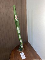 Full view of tall, green stretched 7UP glass art bottle mounted on a base, standing on a wooden surface.