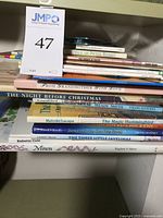 Photo showing a shelf with a total of 22 children's books, including titles such as 'The Tale of Peter Rabbit,' 'The Magic Hummingbird,' 'The Three Little Javelinas,' and 'The Night Before Christmas.' The books are stacked in two rows with visible spines and some titles easily readable.