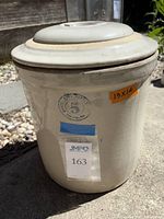 Front view of the antique stoneware crock with sticker labels and visible chip near the top edge.