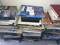 Photo of stacked nearly 100 mostly hardback books, showing diversity in art, design, and American landscape titles.