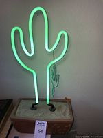 Lit neon cactus light glowing green in faux-terra cotta planter base with sand and green painted barbed wire ornament.