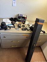 Overview shot showing multiple items including Maxxim Dynex camera with Sigma zoom lens, Fujifilm FinePix A825 camera with box, various accessories, and DaLite projector screen case standing upright.