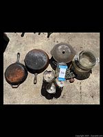 Top-down photo showing three cast iron pans, painted iron Christmas tree, and clear glass containers and bowls on concrete floor.