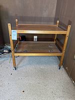 Front view of the BRDR FURBO two-tier wooden TV cart on casters showing the lower shelf with black residue and the upper shelf with corner posts.