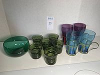 Overview of the full lot with six green candle holders, four soda glasses (2 blue, 2 purple) and emerald green bowl