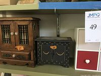 Three decorative storage items on a shelf: wooden jewelry box, black celestial design box, small cubic storage unit with red and white drawers with heart knobs