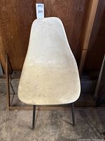 Front view of beige fiberglass molded chair shell with black metal legs showing wear and dirt.