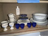 Shelf view of cups stacked and stacked plates alongside cobalt blue bowls and glass containers with lids
