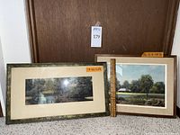 Two framed landscape art prints leaning against a door with a measuring stick indicating sizes.