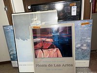 Four framed art posters including three gallery exhibition posters and one abstract poster leaned against a wall.