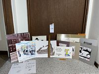 Photo showing the full lot of mixed art pieces including framed and unframed prints and drawings spread on carpet near a wooden door.