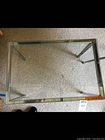 Top view of rectangular metal frame table with clear glass top on beige carpet, showing full surface and frame edges