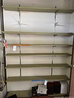 Full view of seven green shelves mounted on two vertical metal brackets fixed to wall