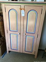 Front view of the wooden cabinet showing two doors with hand-painted peach and multicolor accent panels and white knobs.