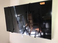 LG 43-inch TV displayed showing screen and cables, with wall mount hook visible underneath, reflecting nearby light and furniture.