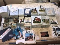Overview of 10 Harbour Lights lighthouse miniatures, their original boxes, booklets, newsletters, and collection materials spread out on a mattress.