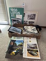 Collection of Lotus memorabilia including 1956 Lotus XI booklet, Historic Lotus and Elite Lotus magazines, black and white vintage photos, and Lotus racing t-shirt or cloth, all displayed together.