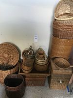 Multiple stacks and piles of woven baskets of various sizes and shapes, showing quantity and condition.
