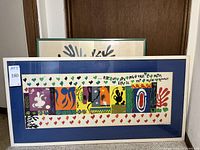 Large white-framed horizontal print with colorful cut-out compositions and hearts border; green-framed leaf silhouette print visible behind