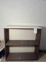 Front view of a two-shelf wood bookshelf with a white painted top plank and open shelves with visible scratches and marks.