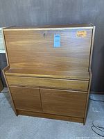 Closed view of Danish teak veneer desk with fold-down writing surface in the upright locked position showing exterior wood grain finish and bottom cabinet doors.
