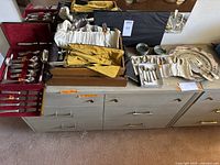 Wide view of the various flatware, utensils, cases, wine coasters, plates, and miniature box arranged on a dresser.