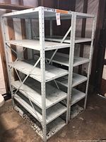 Two gray metal shelving units with five shelves each, assembled and standing side by side in a wooden enclosure.