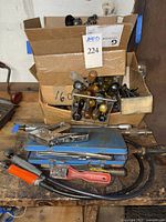 Mixed hand tools with screwdrivers, staple guns, and other tools stacked on a workbench inside open boxes.