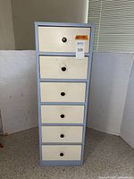 Front view of the 6-drawer narrow solid wood storage unit painted in gray and ecru, showing the drawers and round knobs.