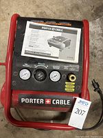 Top view of Porter Cable C1010 compressor control panel with pressure gauges, regulator knob, brand label and instruction manual on top.