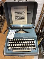 Blue Remington Personal-Riter portable typewriter in open protective hard case with instruction manual and cover visible