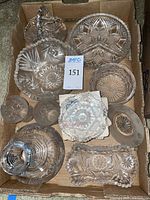 Eight pieces of cut glass arranged in a cardboard box featuring bowls, pitcher, plates, and serving dishes with starburst and geometric cut patterns.