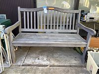 Full front view of the teak outdoor bench showing leaf carving on the backrest and slatted seat with armrests.