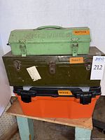 Front view of three stacked toolboxes: green metal on top, dark brown metal middle, and orange plastic bottom.