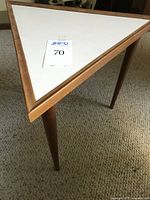 Triangular side table showing white top with wooden trim and three legs.