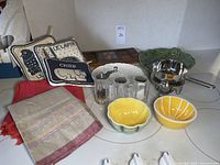 Overview photo showing all items in the lot including fondue pot, hot pads, ceramic bowls, serving plates, salt and pepper shakers, and linens.