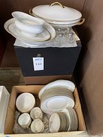 Photo showing covered serving dish, gravy boat with saucer, several plates on black box and boxed smaller plates and bowls below