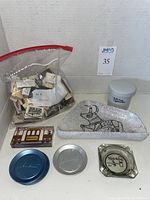 Overall lot contents showing bag of souvenir matches, ceramic ashtray with bull design, glass 'Kitchen Cigarettes' ashtray, and three metal trays.