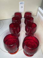 Eight ruby red juice glasses arranged in two rows with a view from above and front, showing hexagonal pattern bases.