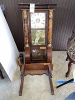 Full view of vintage Seth Thomas wall clock disassembled with wooden stand in front, showing decorative columns and painted glass panel.