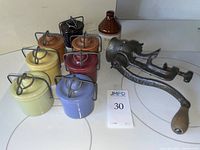 Photo showing eight vintage stoneware crocks in different colors with metal lid clamps, one brown and white 'MERCURY' jug, and an antique Eclipse meat grinder with wooden handle.