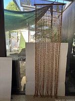 Full view of vintage wood bead curtain hanging against a window, showing vertical strands hanging from a horizontal wooden bar.