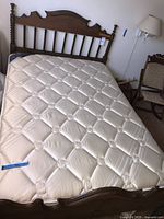 Full view of vintage full/double wood bed frame with tufted cream mattress showing spindled headboard and curved footboard.