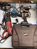 Variety of power tools on table including red Chicago Electric reciprocating saw, cordless drills, battery chargers, and a carrying case