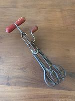 Top view of antique hand crank mixer showing metal beaters and red wooden crank handle.