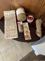 Burlap craft supplies including alphabet stickers, burlap ribbon rolls, decorative flowers, twine, and red string ribbon displayed on a dark table.