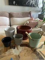 Photo showing the collection of five assorted small plant pots in various colors and materials on a wooden table.