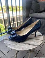 Side view of navy peep-toe heels with bow detail, showing heel height and patent finish.