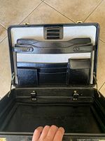 Open view of the briefcase showing pen holders, card slots, and coin pouch against light interior lining with minor wear on the interior base.