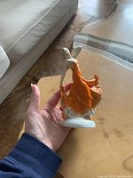 Photo of a hand holding the dancing lady figurine, showing the orange dress, white base, and detailed face and hair.
